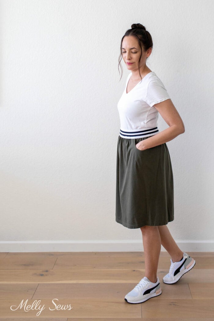Brunette woman in white t-shirt and olive knit skirt outfit with sneakers