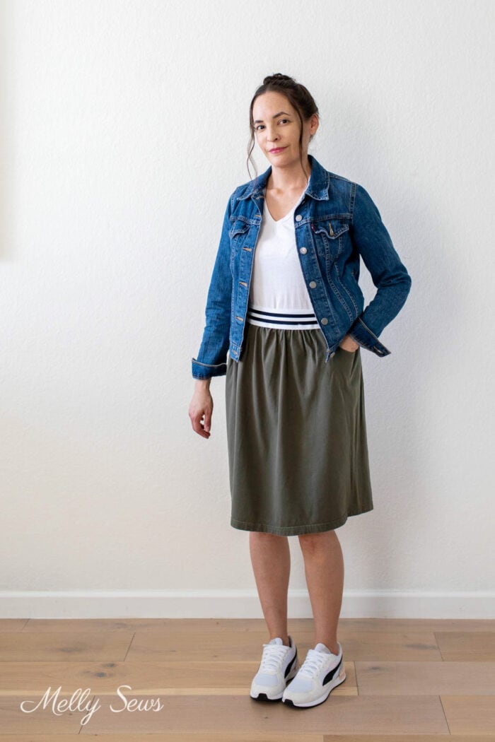Woman in jean jacket with hand in pocket of her olive fabric skirt