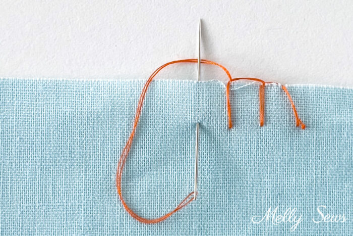 How to sew a blanket stitch - an example of a blanket stitch sewn in orange thread on blue fabric
