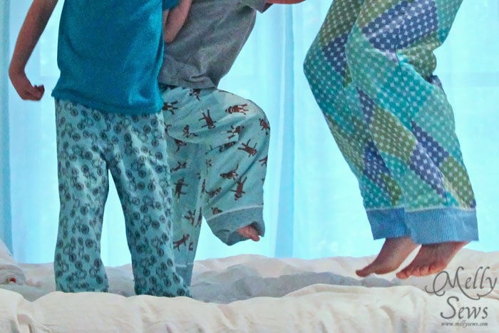 children and woman's legs wearing handmade pajama pants and jumping on a bed 