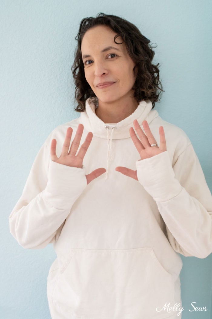 Smiling woman wearing ivory sweatshirt with thumbholes in the sleeves
