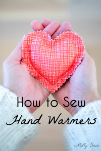 Hands holding a heart shaped DIY hand warmer sewn in coral colored fabric