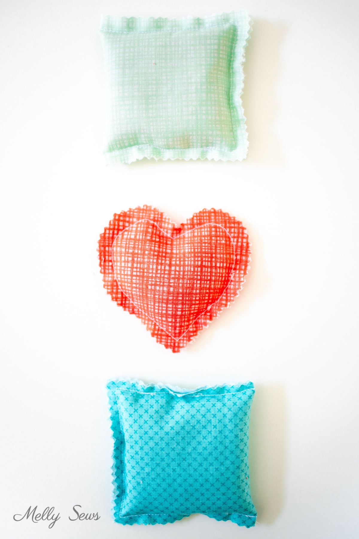Three rice filled hand warmers in mint, red heart and turquoise cotton prints with pinked edges stacked on white