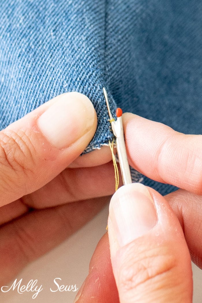 The pointed end of a seam ripper taking out a single stitch in a seam