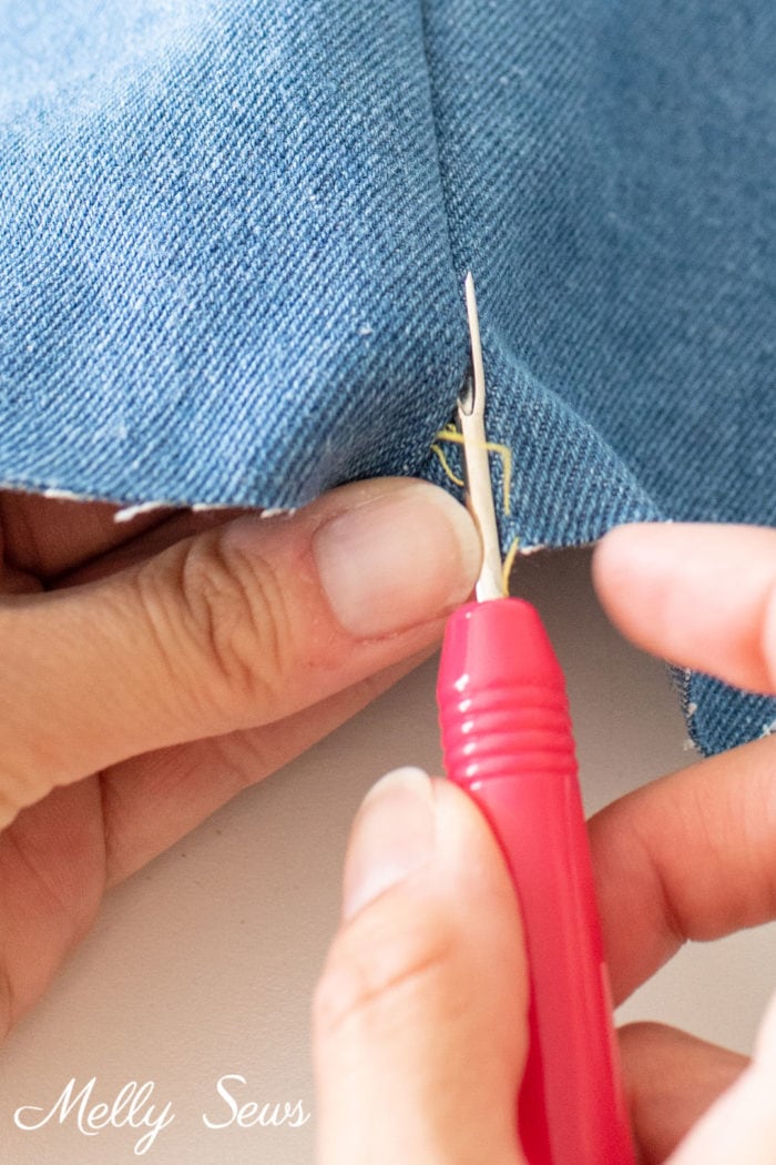Seam ripper being pushed through a seam to remove stitches quickly