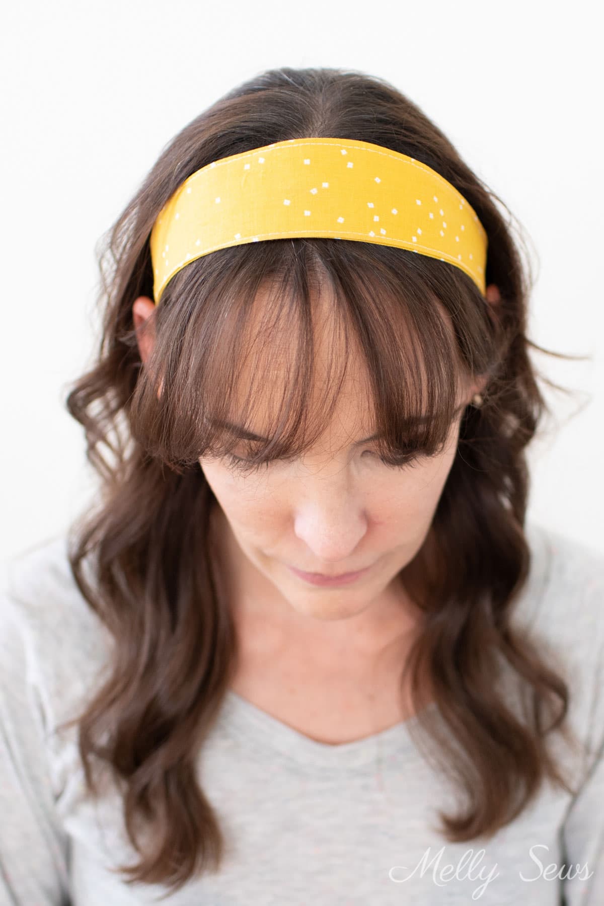Woman with dark brow hair wearing a gold colored fabric headband