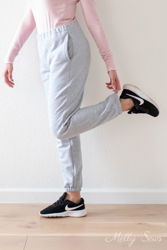 Woman's legs in gray joggers as she touches the ankle elastic on one leg