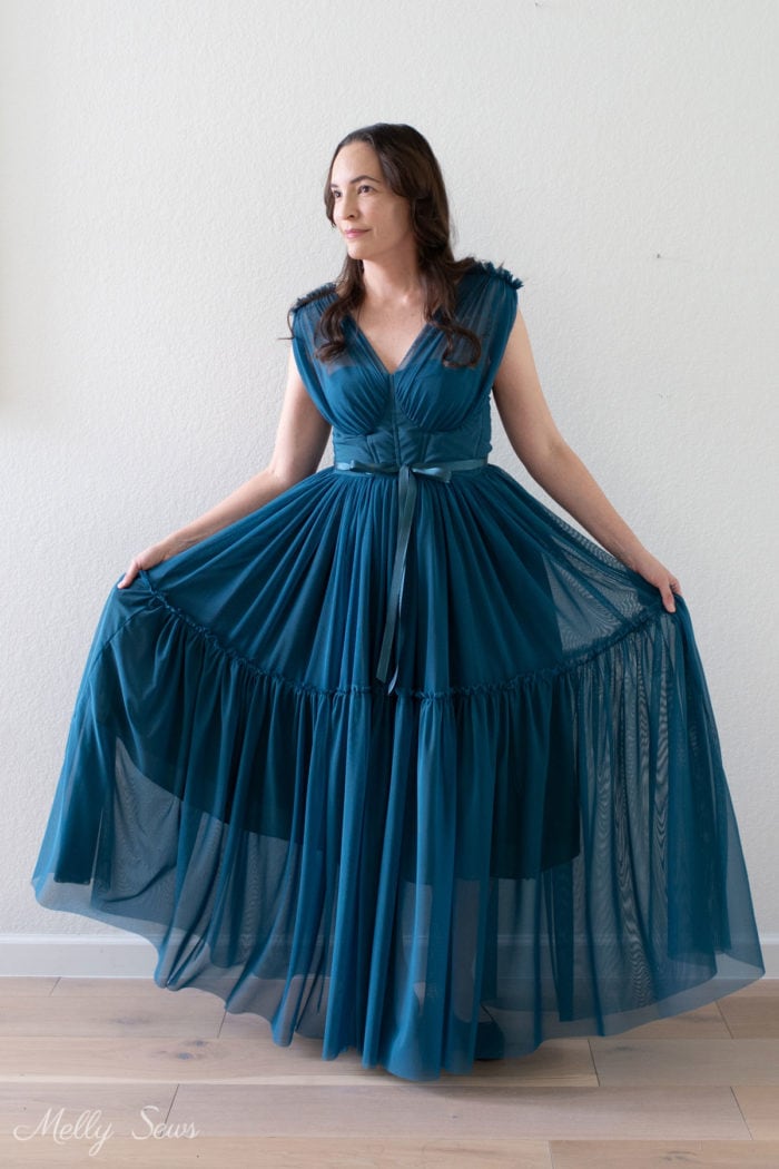 Woman with dark brown hair wearing a full length formal teal dress that she sewed with a sheer overskirt