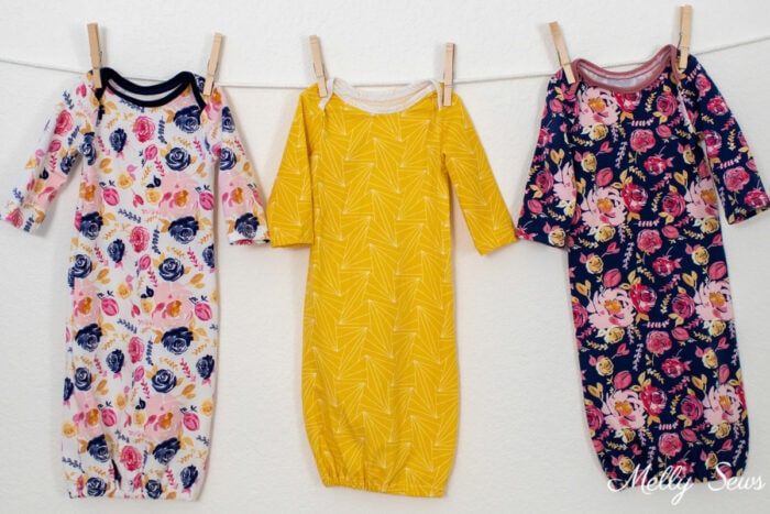 Three baby gowns on a clothesline, one in white floral, one in a yellow geometric print, and one in a navy blue floral