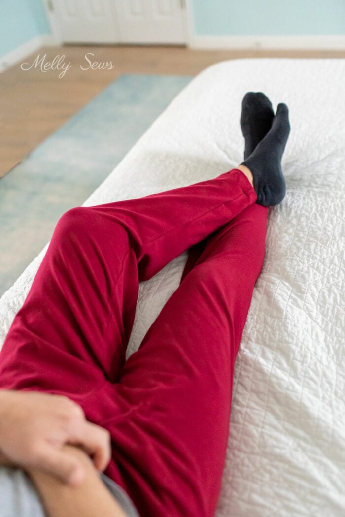 Man's legs clad in home sewn maroon lounge pants sitting on a bed