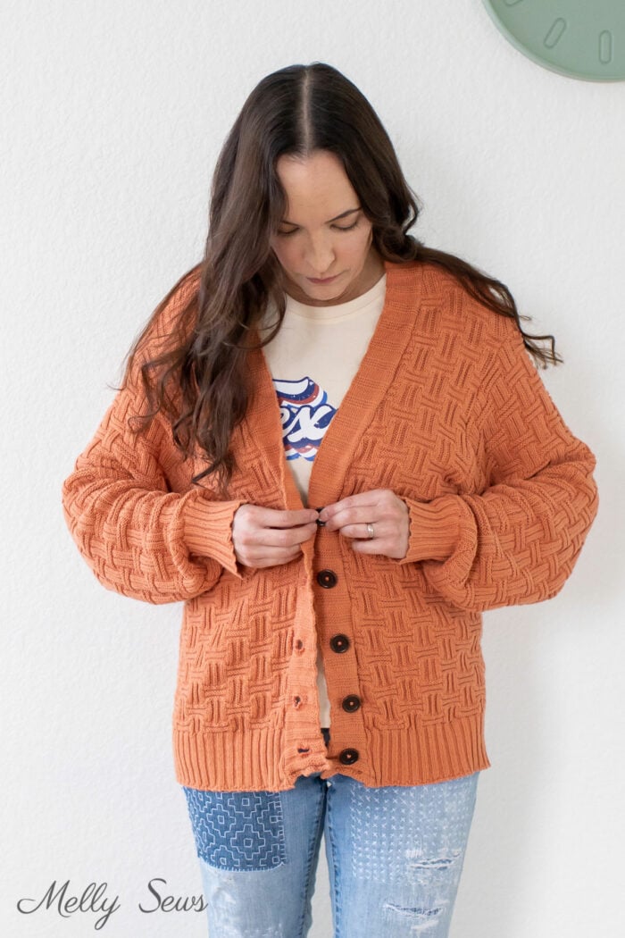 Woman buttoning up a cardigan she sewed from a throw blanket
