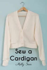 Ivory cardigan hanging on a light blue wall with the text Sew a Cardigan