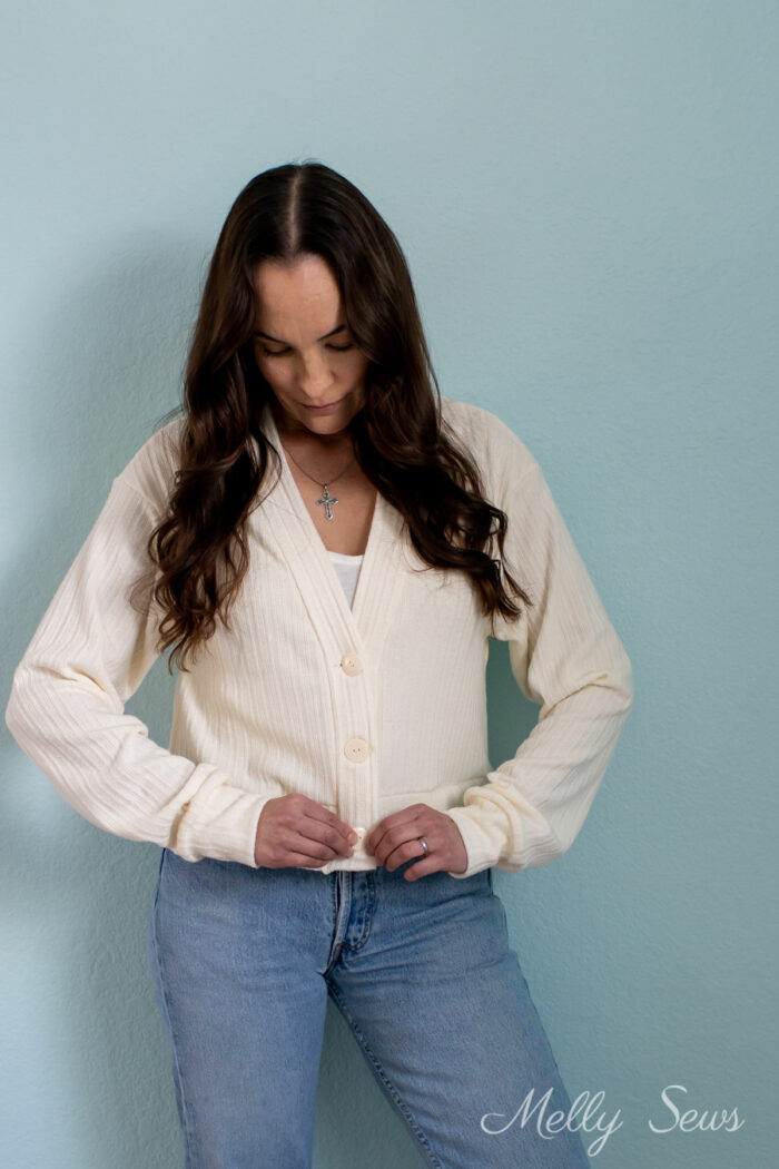Brunette woman buttoning the bottom button of a sweater she made