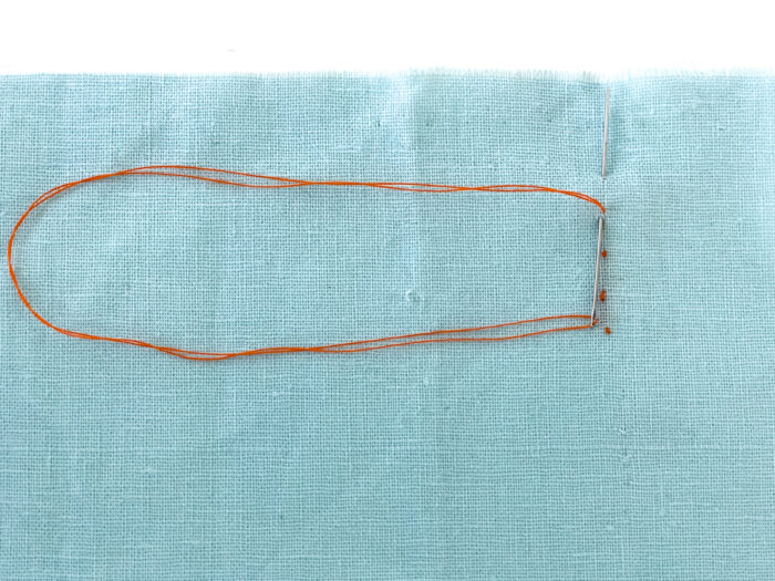 Small backstitches in orange thread on blue fabric