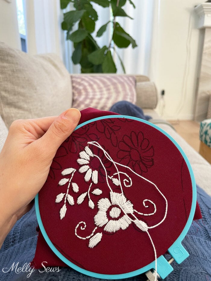 White floral embroidery on dark red fabric in an embroidery hoop