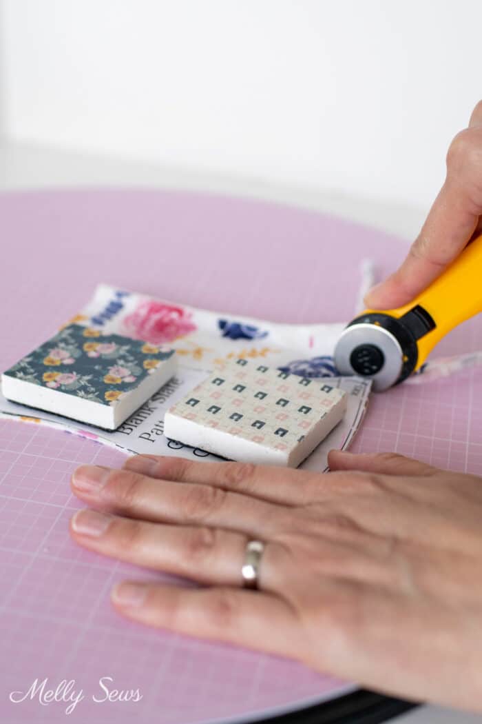 Woman's hands using a small rotary cutter on a pad to cut out a pattern