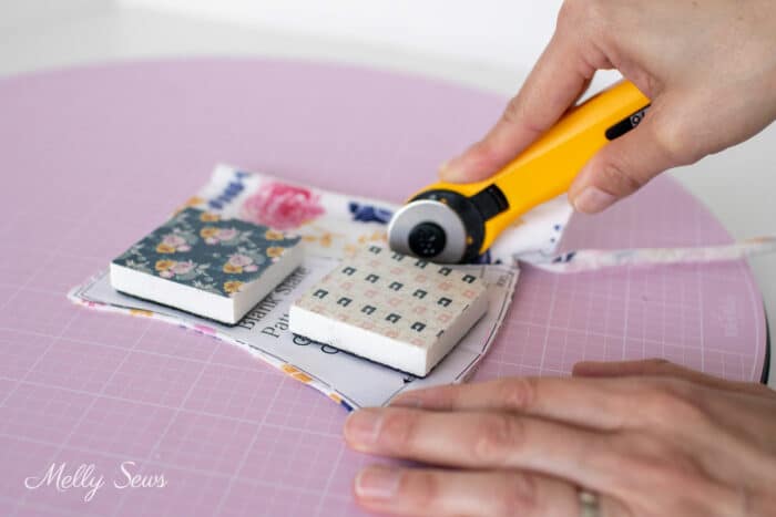 Woman's hands using a 28mm rotary cutter to trim fabric on a mat