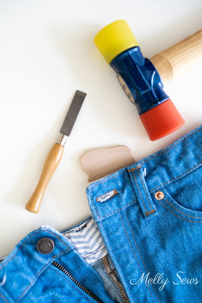 Sewing notions - a chisel for buttonholes and a mallet on a table next to a pair of jeans