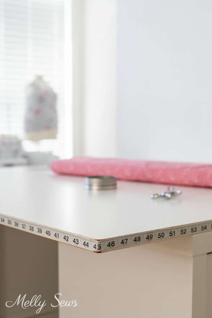 Cutting table in a sewing room with measuring tape along the edge.