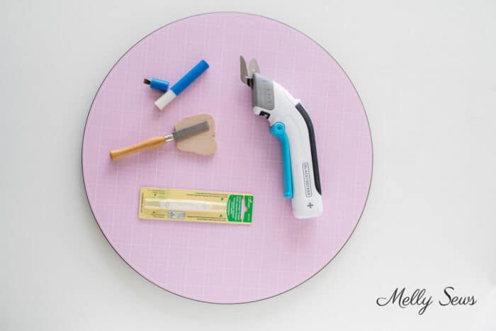 Electric scissors, buttonhole chisel, needle threader and sewing machine screwdrivers on a rotating cutting mat 