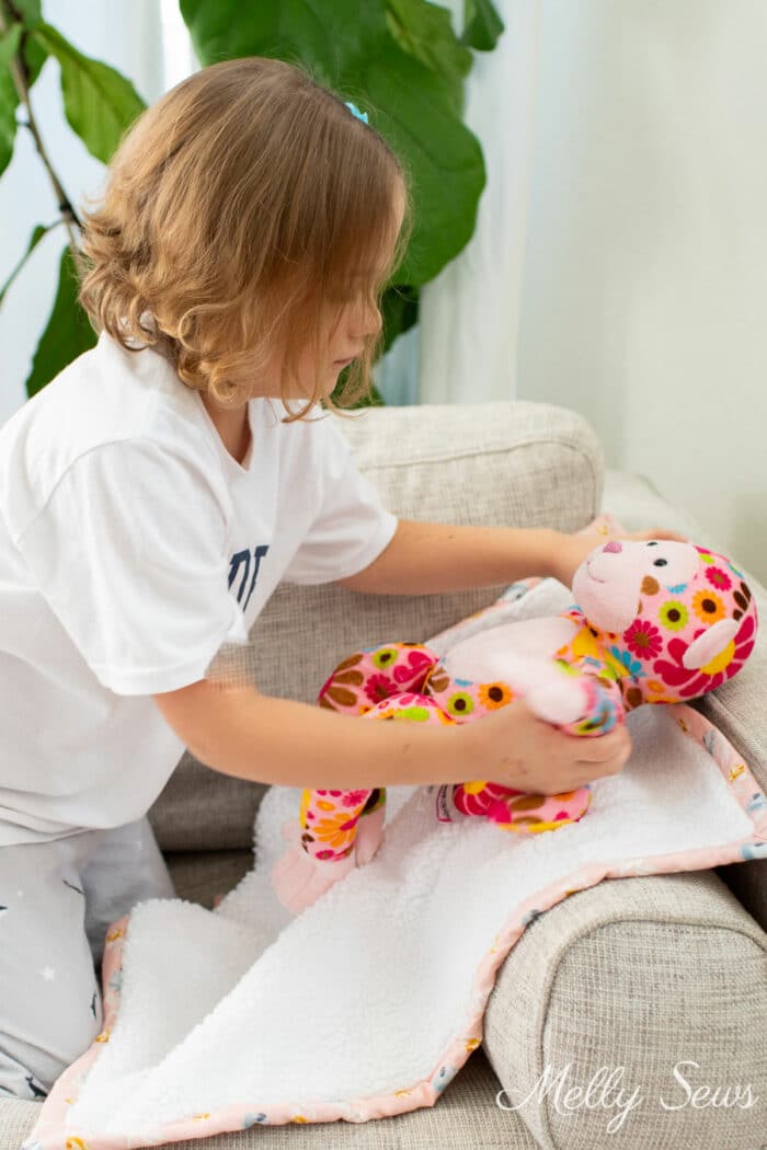 Young girl placing a stuffed animal on a fuzzy blanket