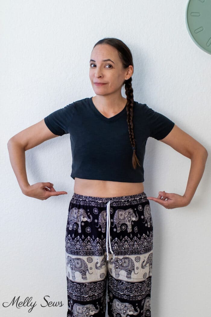 Women in a cropped black t-shirt and printed pants points at her waist