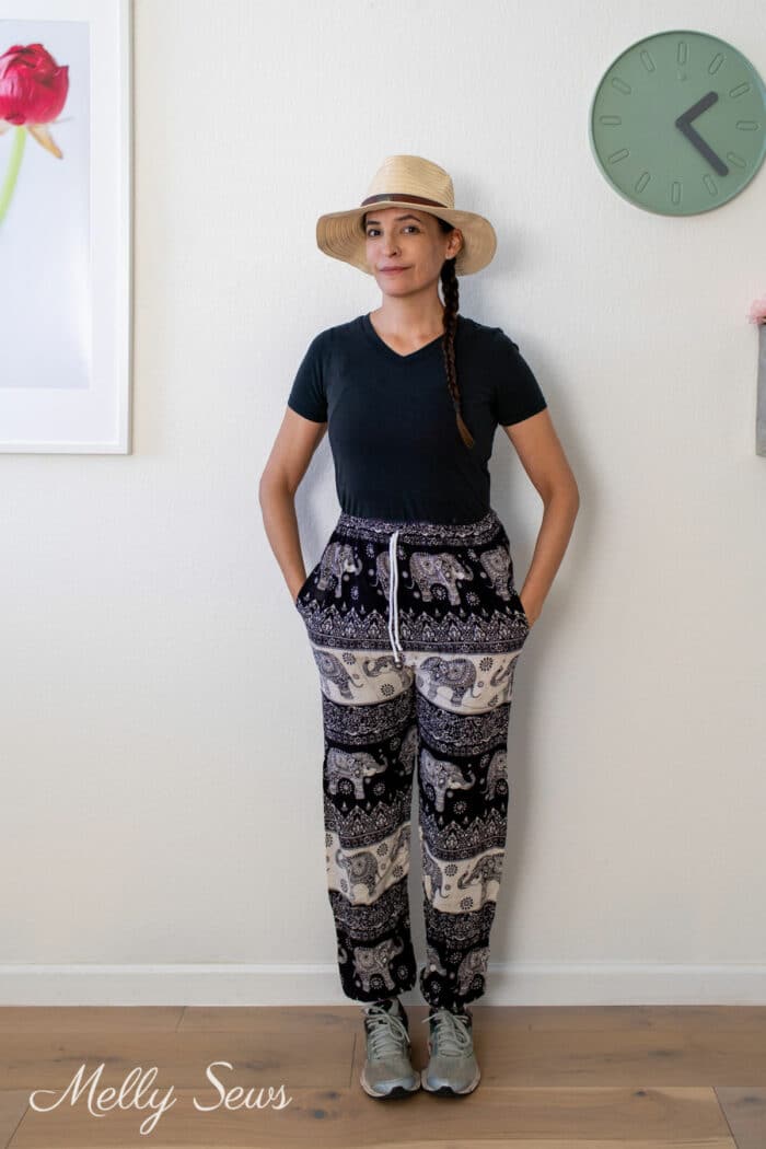 Woman wearing a straw hat, black t-shirt, and printed elephant pants with running shoes