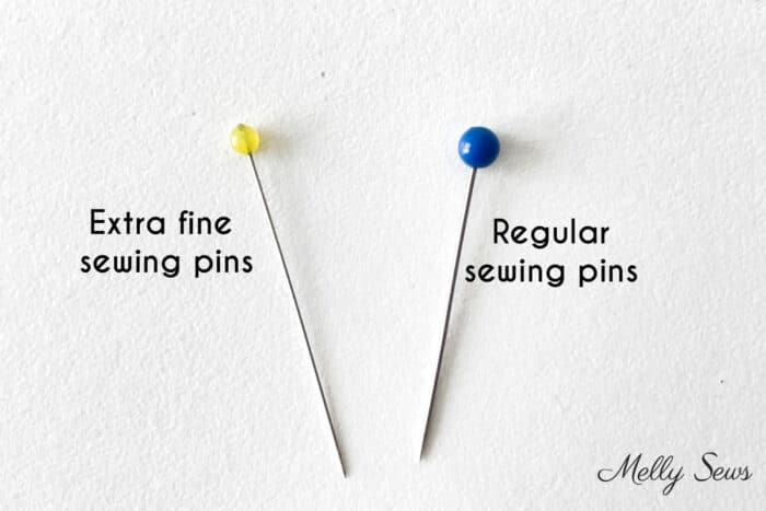 A single extra fine width sewing pin next to a single regular width sewing pin