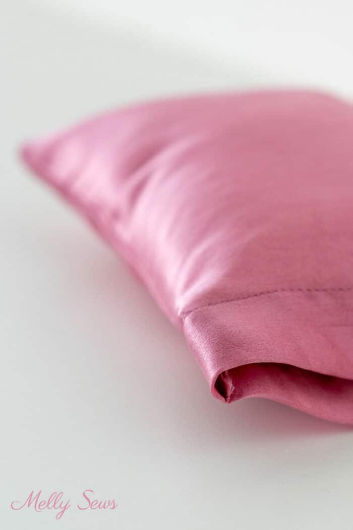 Corner of a pink silk pillowcase sewn at home in the foreground with the rest of the pillow blurring off toward the background
