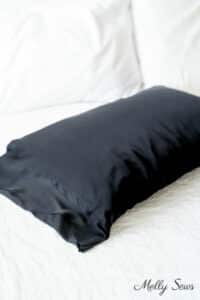 Soft light emphasizing the drape of a black silk pillowcase on a pillow laying on white cotton bedding