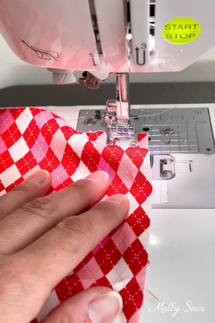 Hand pushing red and pink diamond check spring fabric under a sewing machine needle