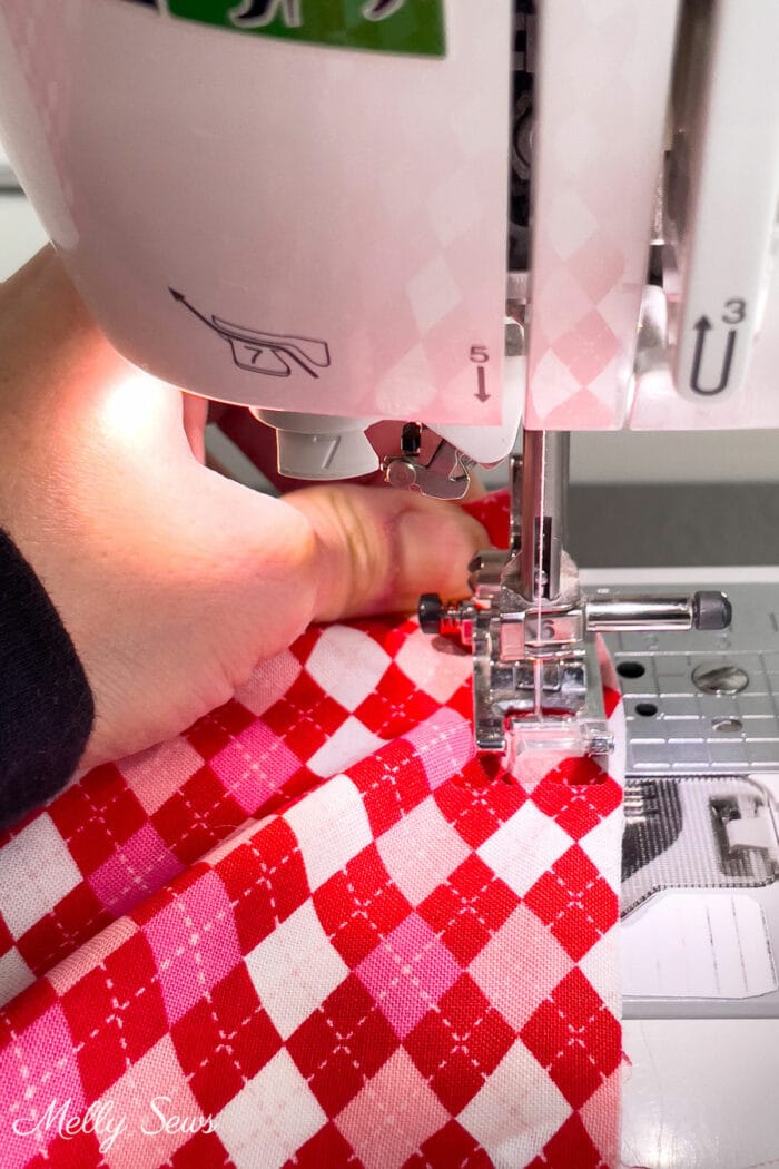 Hand pulling red and pink diamond check spring fabric under a sewing machine needle