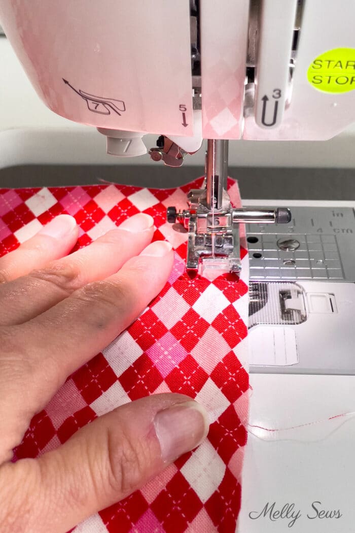 Hand feeding red and pink diamond check spring fabric under a sewing machine needle