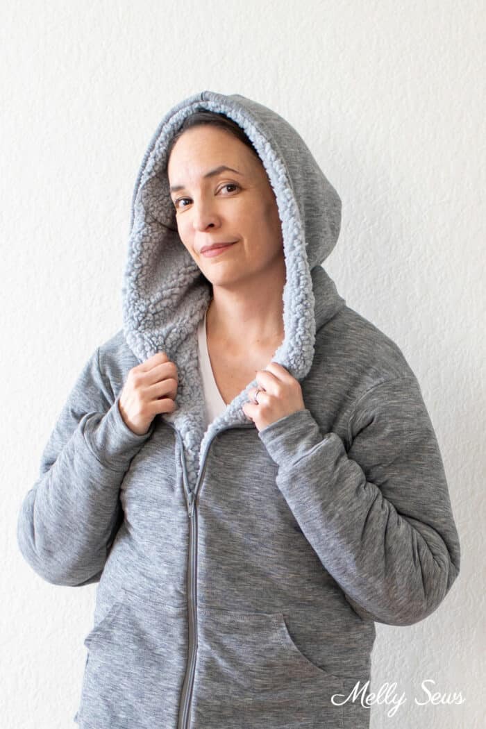 Woman in a zipped up gray hooded jacket holding on to edges of hood where fuzzy lining peeks out