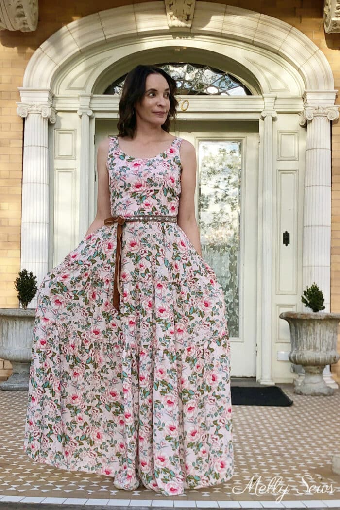 Woman in a pink floral gown stands in front of an old mansion