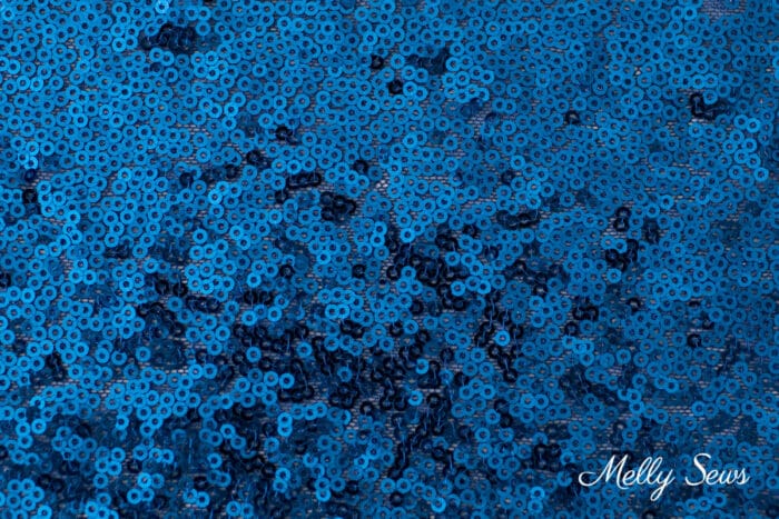 Blue sequin fabric close up showing tiny randomly sewn sequins.