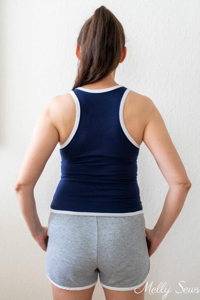 Back view of a brunette women wearing a navy blue racerback tank top and gray shorts, both with white trim
